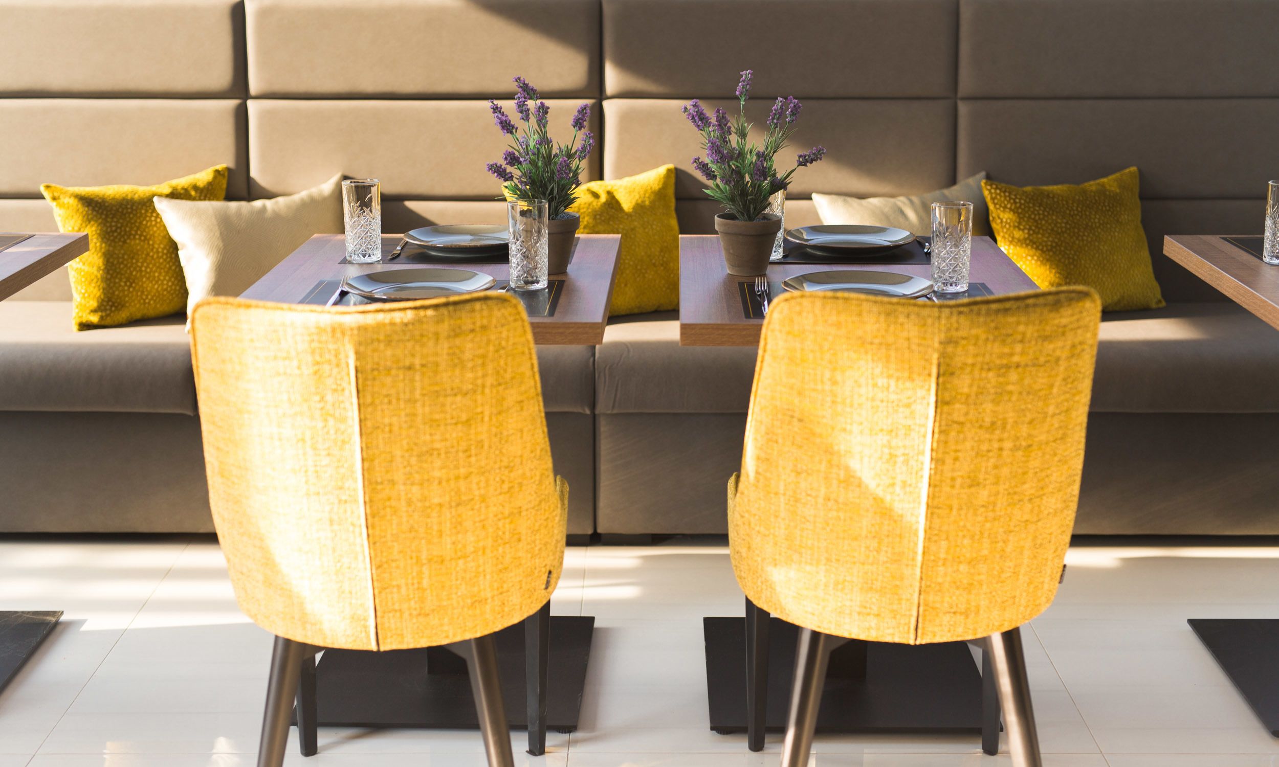 Un comedor moderno con dos sillas amarillas, un sofá y una mesa dispuesta para dos personas.