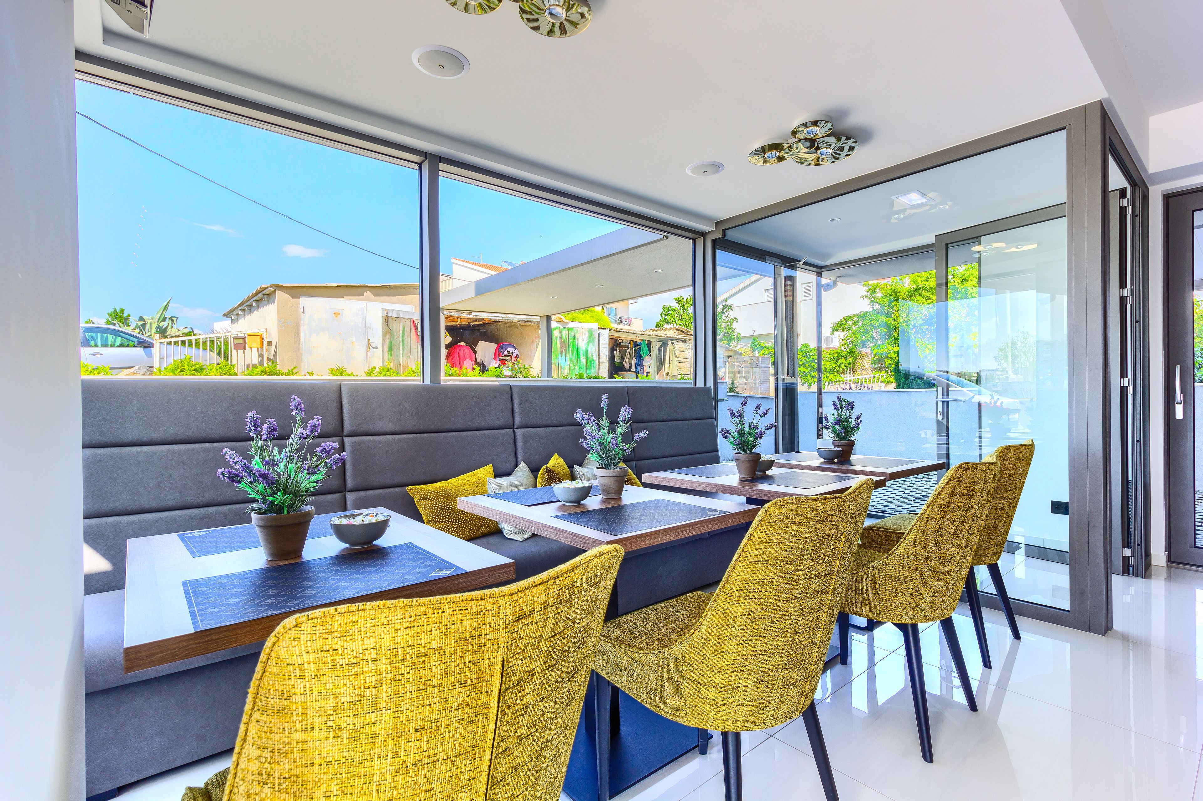 A modern dining area with a large window, a sofa, and yellow chairs.