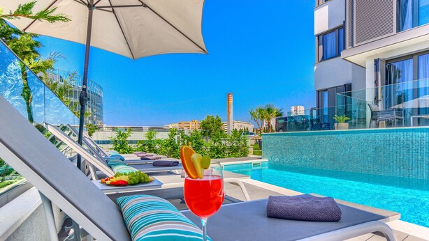 A poolside lounge with a glass balustrade, a red cocktail with a garnish, and a clear blue sky. - Bel Residence (Split)