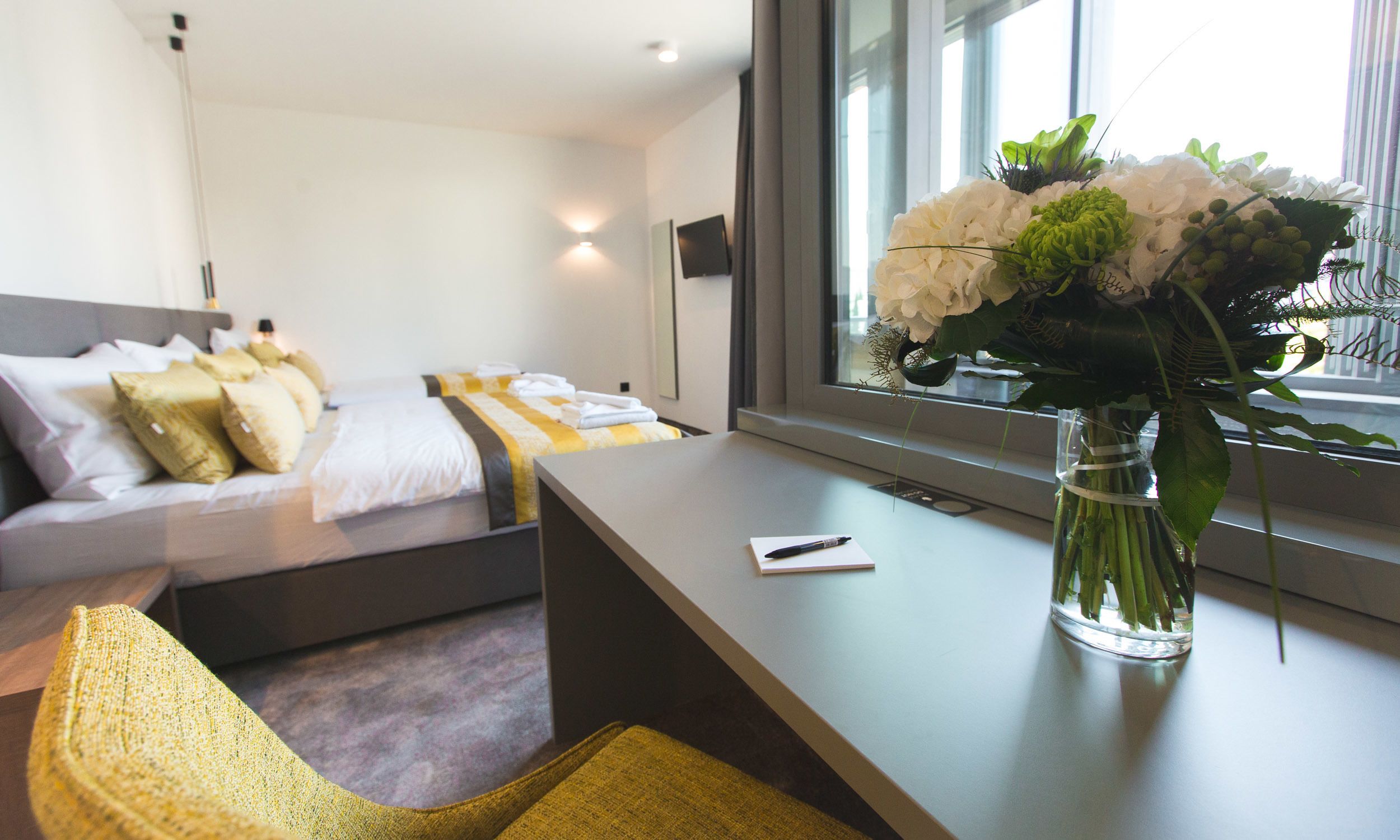 A modern hotel room with a bed, bedside table, and a vase of flowers.