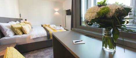 A modern hotel room with a bed, bedside table, and a vase of flowers.