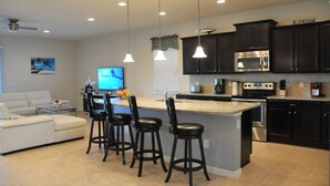 A modern kitchen with dark cabinets, a central island with bar stools, a flat-screen TV, and a ceiling fan. - Shv1206ha - 8 Bedroom Villa In Windsor At Westside, Sleeps Up To 18, Just 7 Miles To Disney (Kissimmee)