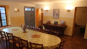 A dining area with a round table, wooden chairs, a buffet station, and a door. - Maison de Veaux (Malaucène)