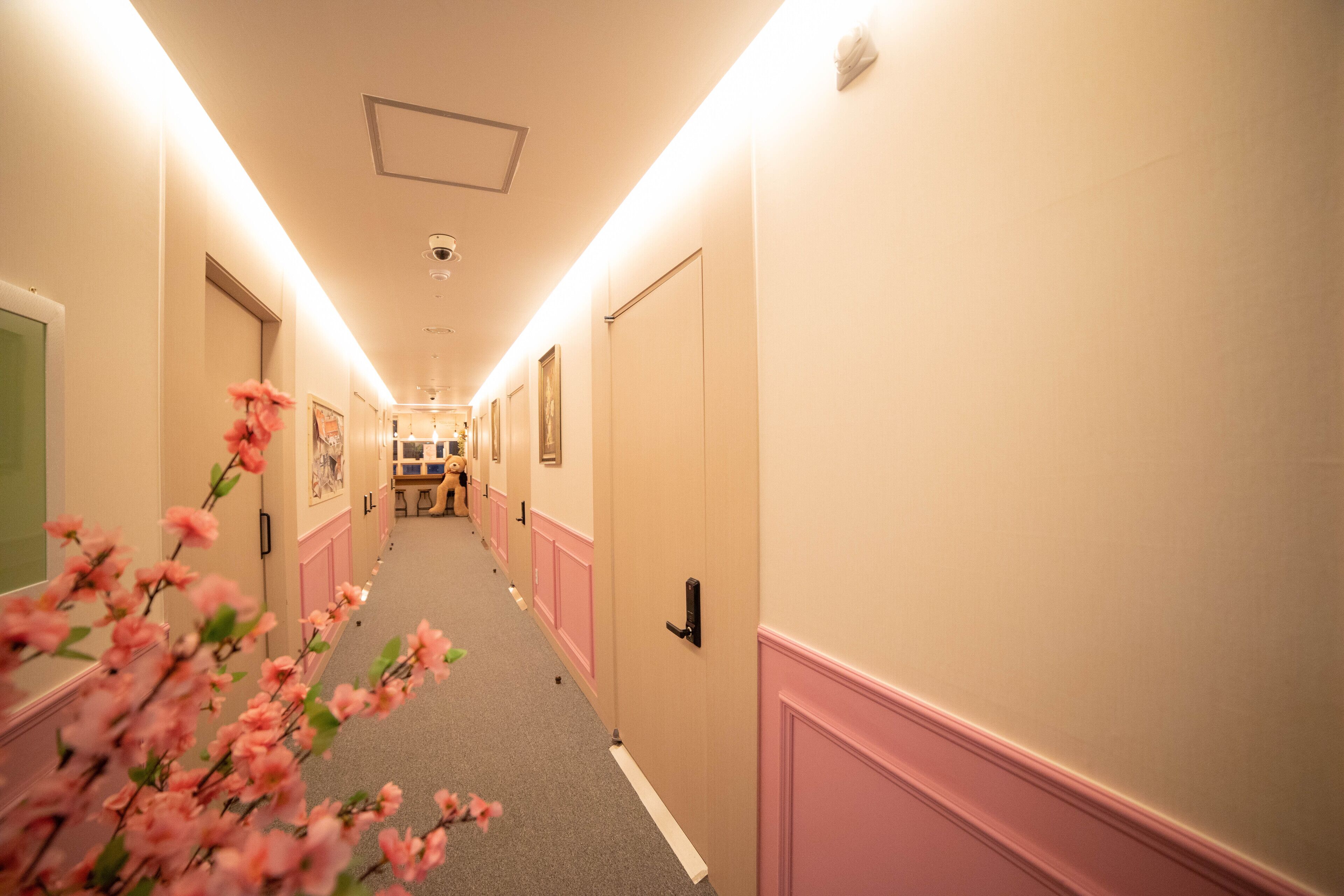 A hotel hallway with a carpeted floor, doors on both sides, and a security camera on the ceiling.