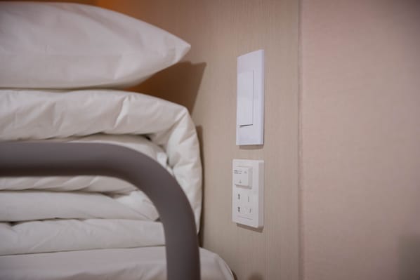 Een net opgemaakt bed met witte lakens en een wandcontactdoos.