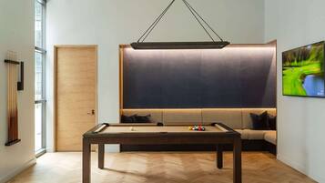 A pool table in a room with a large window, a sofa, and a television.