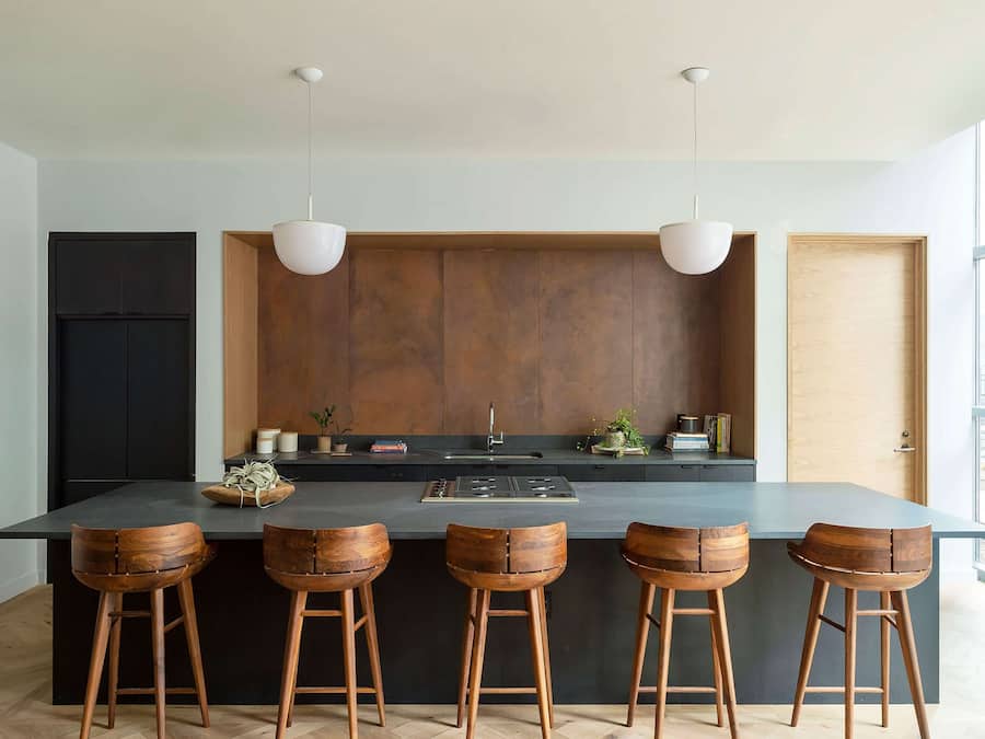 Een moderne keuken met een centraal eiland, vier houten barstoelen en hanglampen.