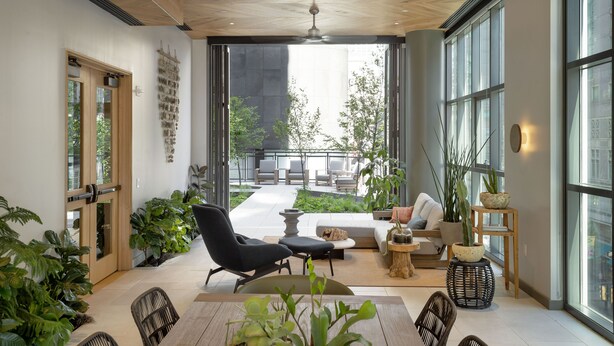 Ein großzügiger Innenbereich mit einem großen Fenster, einem Deckenventilator und unterschiedlichen Sitzgelegenheiten, darunter eine Couch und Sessel.