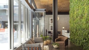 Eine moderne Lobby mit Sitzgelegenheiten, großen Fenstern, einer Ziegelwand und einer grünen Wand.