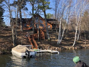 A cabin with a dock extending into a lake, surrounded by trees. - Sunny's Landing 3000 SF home on Prairie Lake (Chetek)