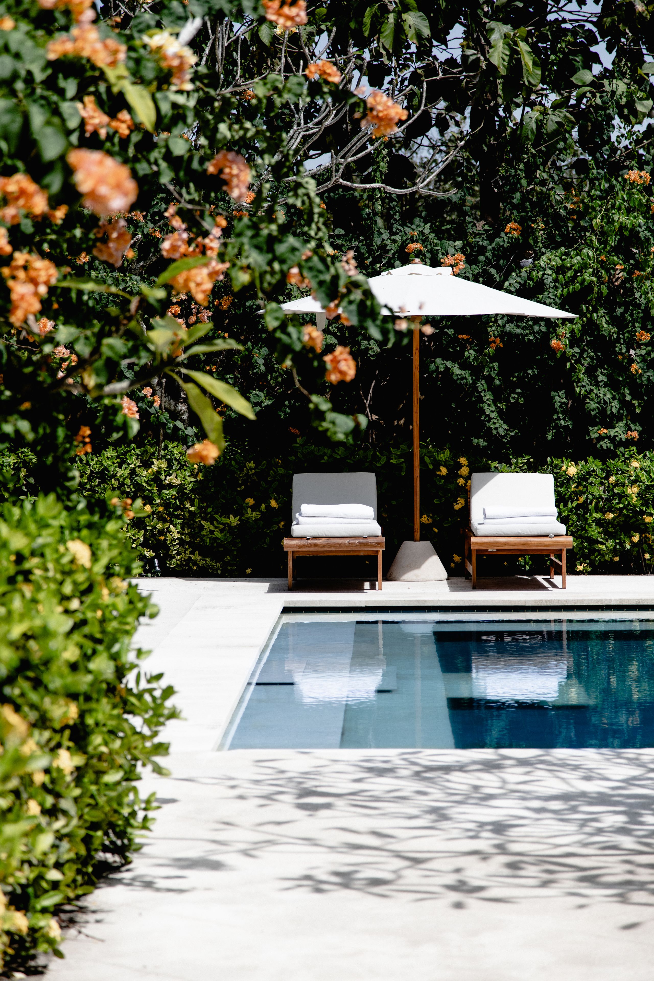 Área da piscina com duas espreguiçadeiras e um guarda-sol branco.