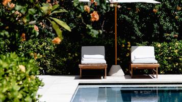Área da piscina com duas espreguiçadeiras e um guarda-sol branco.