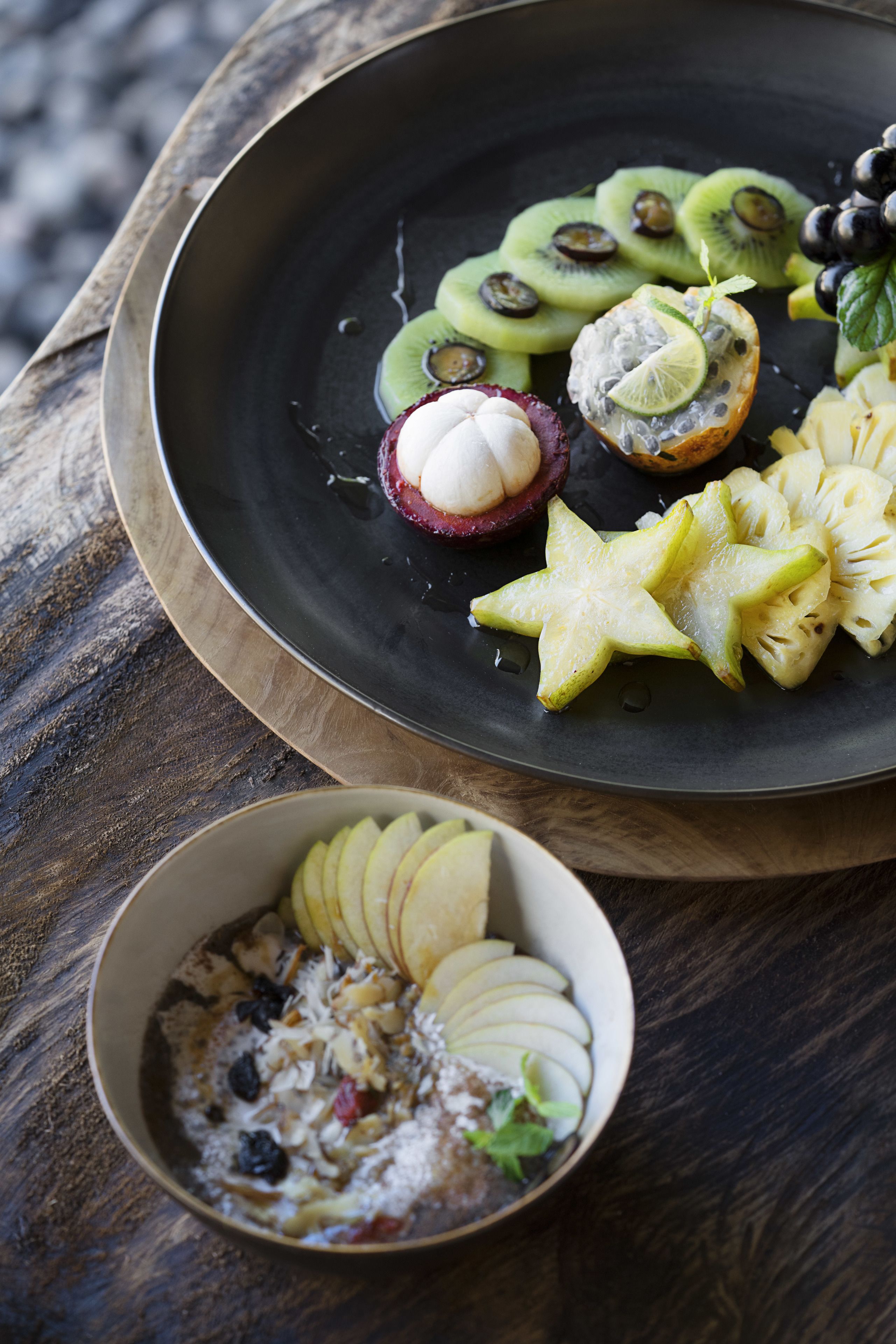 A wooden table with a black plate containing sliced kiwi, a kiwi with lime, and a star-shaped fruit arrangement.