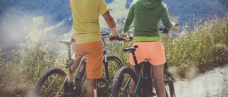 Two people on bicycles on a mountain path with a view of mountains in the background.