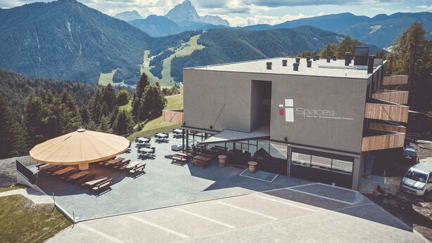 A modern hotel with a flat roof, outdoor seating, and a view of mountains.