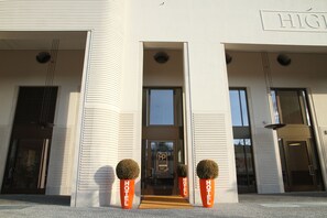 Ein moderner Hotelzugang mit zwei großen Kübelpflanzen, einer Doppeltür und freier Blick auf den Innenbereich durch die Glastüren.