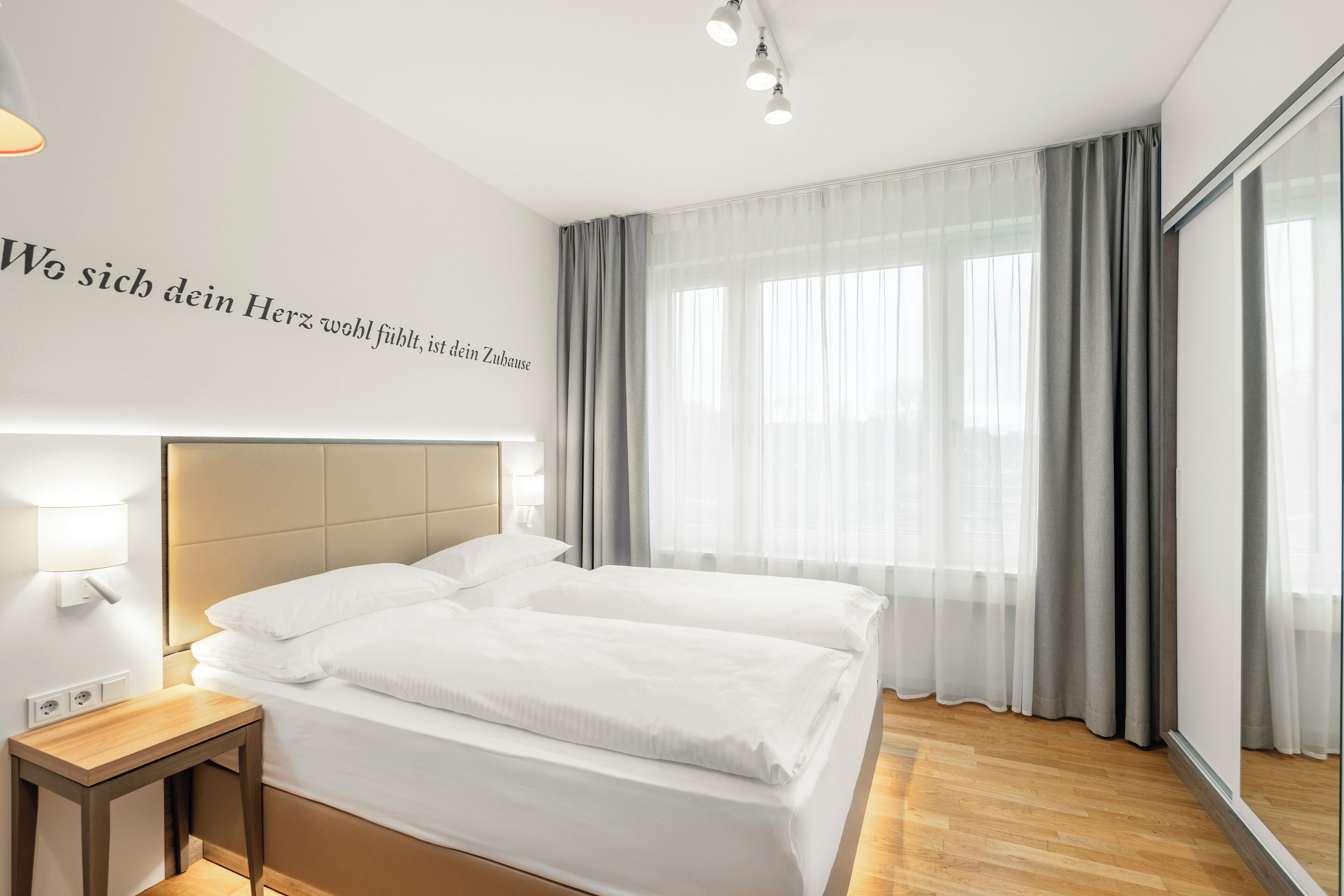 Una habitación de hotel moderna con una cama grande, una mesita de noche y una lámpara fijada a la pared.