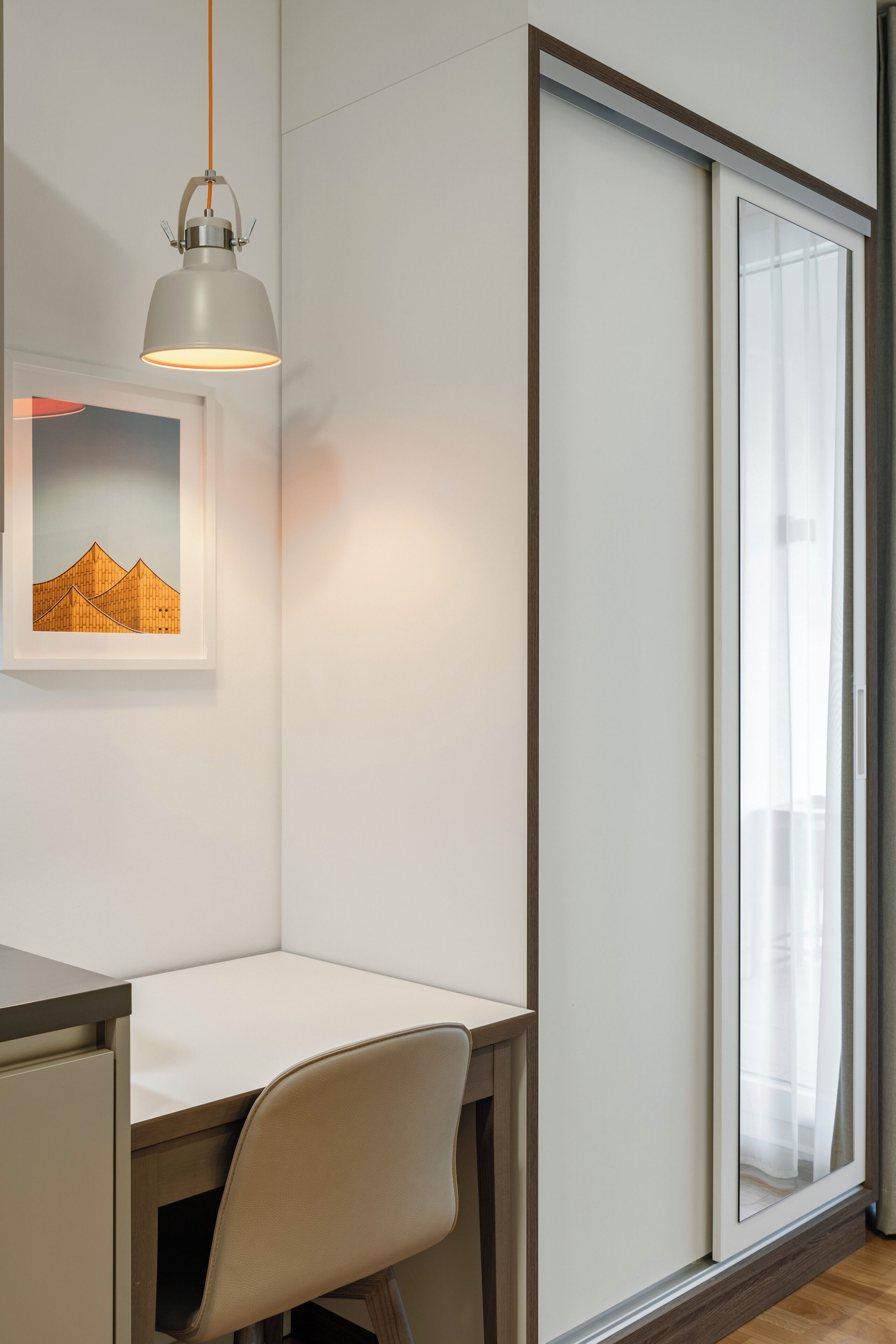 Un espacio de oficina moderno con un escritorio, una silla, una obra de arte enmarcada y una puerta corredera de vidrio.