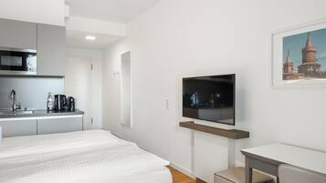 A modern hotel room with a bed, a small desk, a television, and a kitchenette.