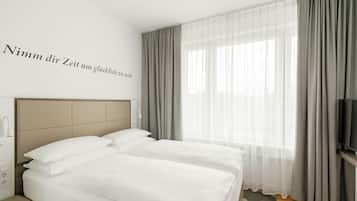 Una habitación de hotel con cama, televisión y ventana con cortinas.