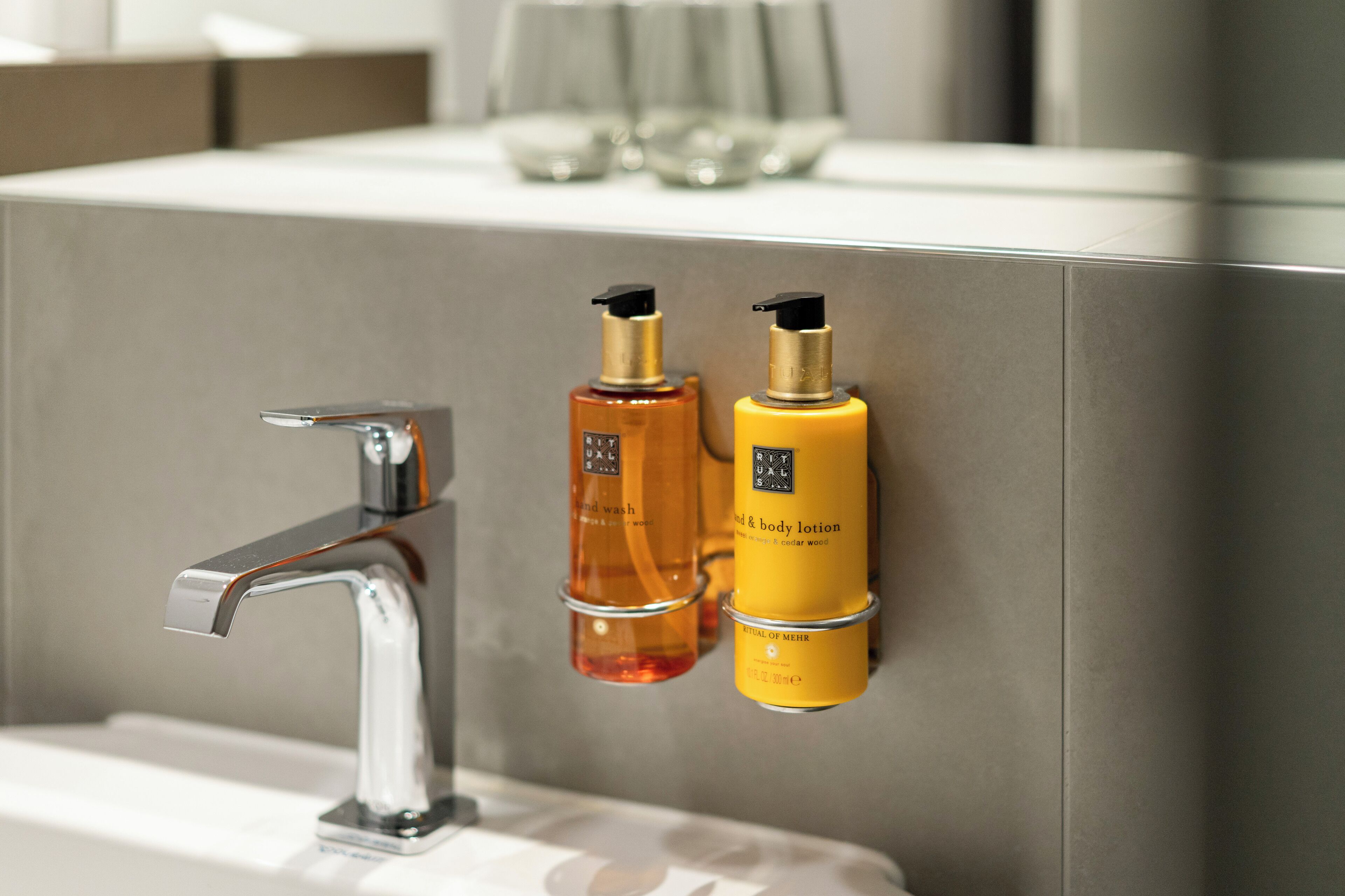 A bathroom with a modern faucet and two bottles of lotion on a wall-mounted holder.
