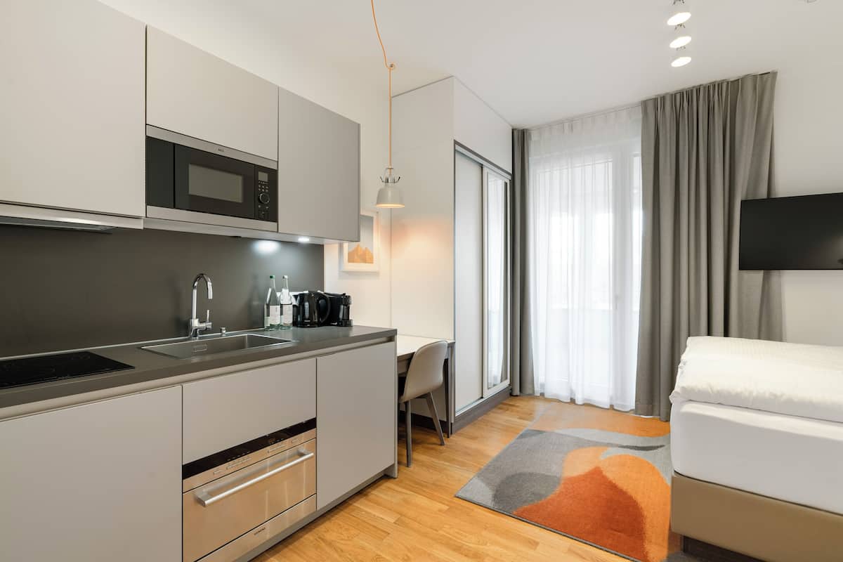 Une cuisine compacte équipée d’un micro-ondes, d’un évier et de placards, un coin repas avec une chaise, et un lit avec un téléviseur.