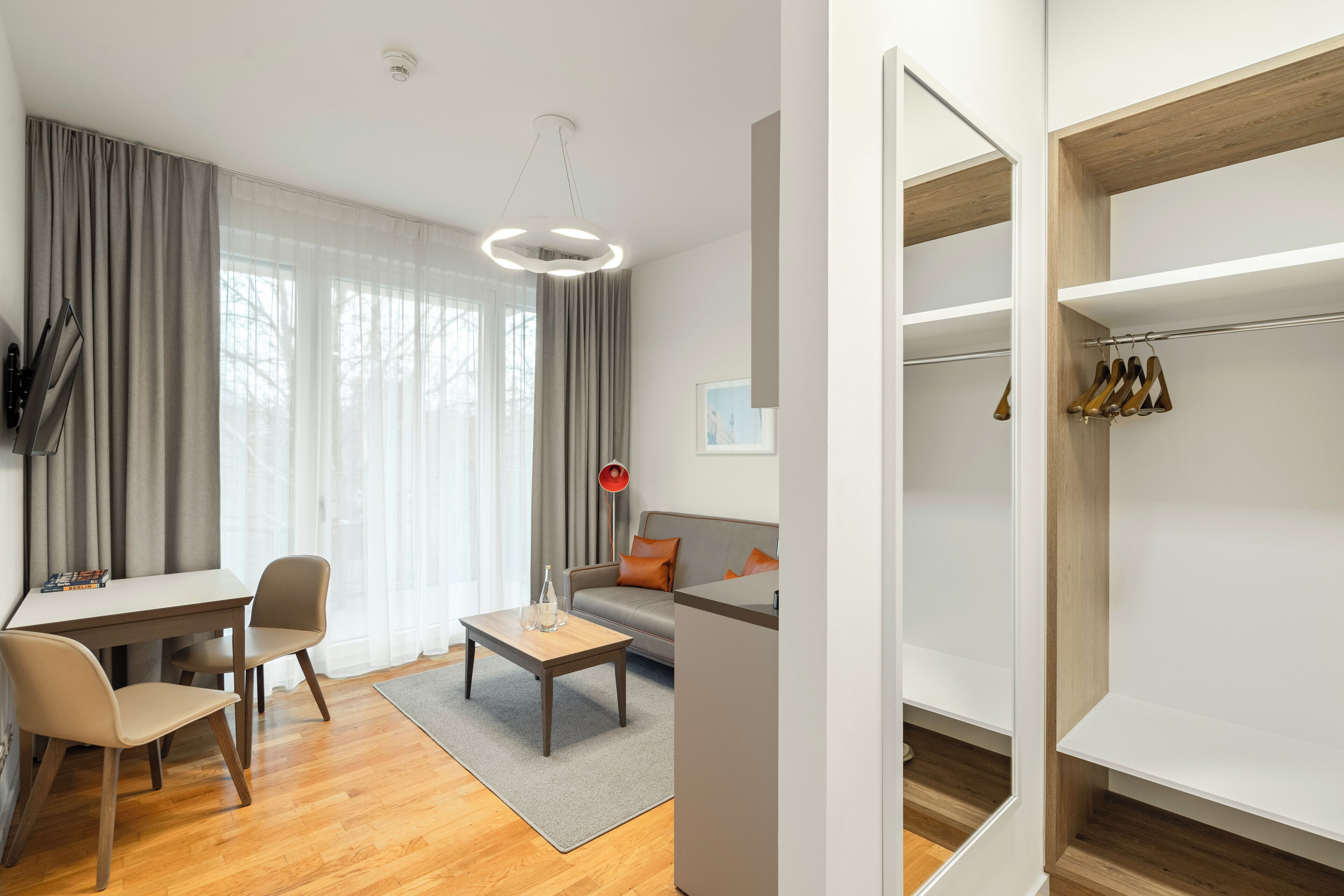 A modern living room with a sofa, coffee table, and chairs. There is a dining area with a table and chairs. The room has large windows with curtains.