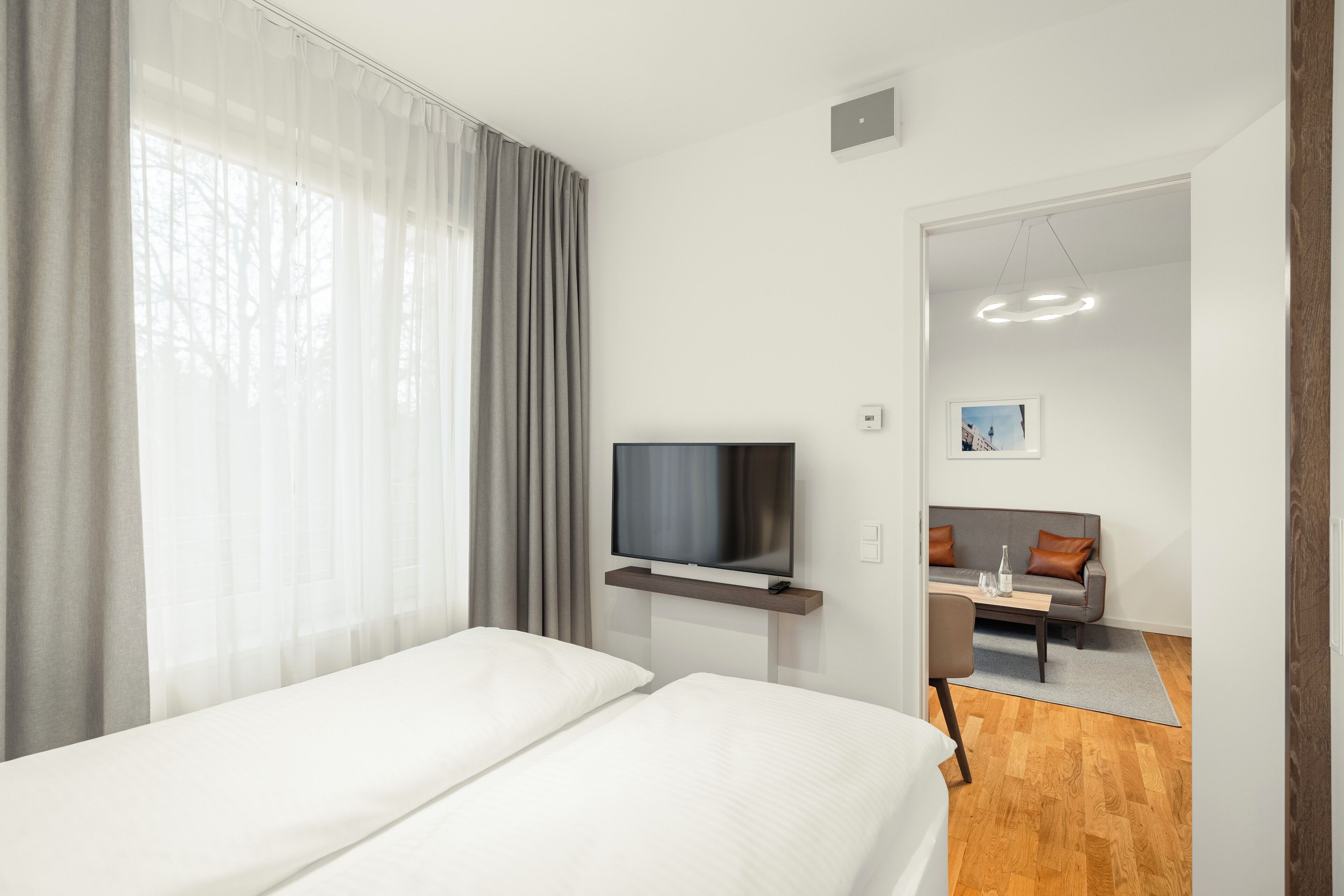 A modern hotel room with a bed, a TV on a stand, a sofa, and a dining table.