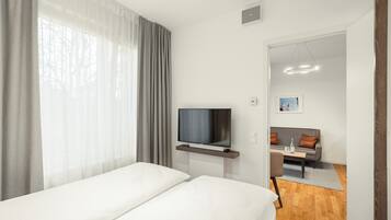 A modern hotel room with a bed, a TV on a stand, a sofa, and a dining table.