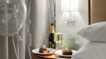 A hotel room with a bed, a nightstand with a bottle of champagne, two glasses of champagne, and two plates of dessert.
