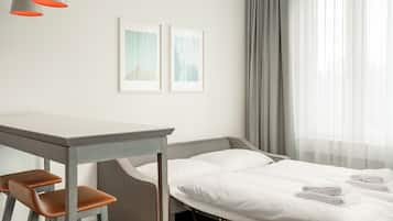 A hotel room with a bed, a desk, two chairs, and two framed pictures on the wall.