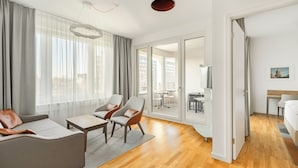 Une chambre d’hôtel moderne, dotée d’un canapé, de fauteuils, d’une petite table et offrant une vue sur la ville grâce à de grandes fenêtres.