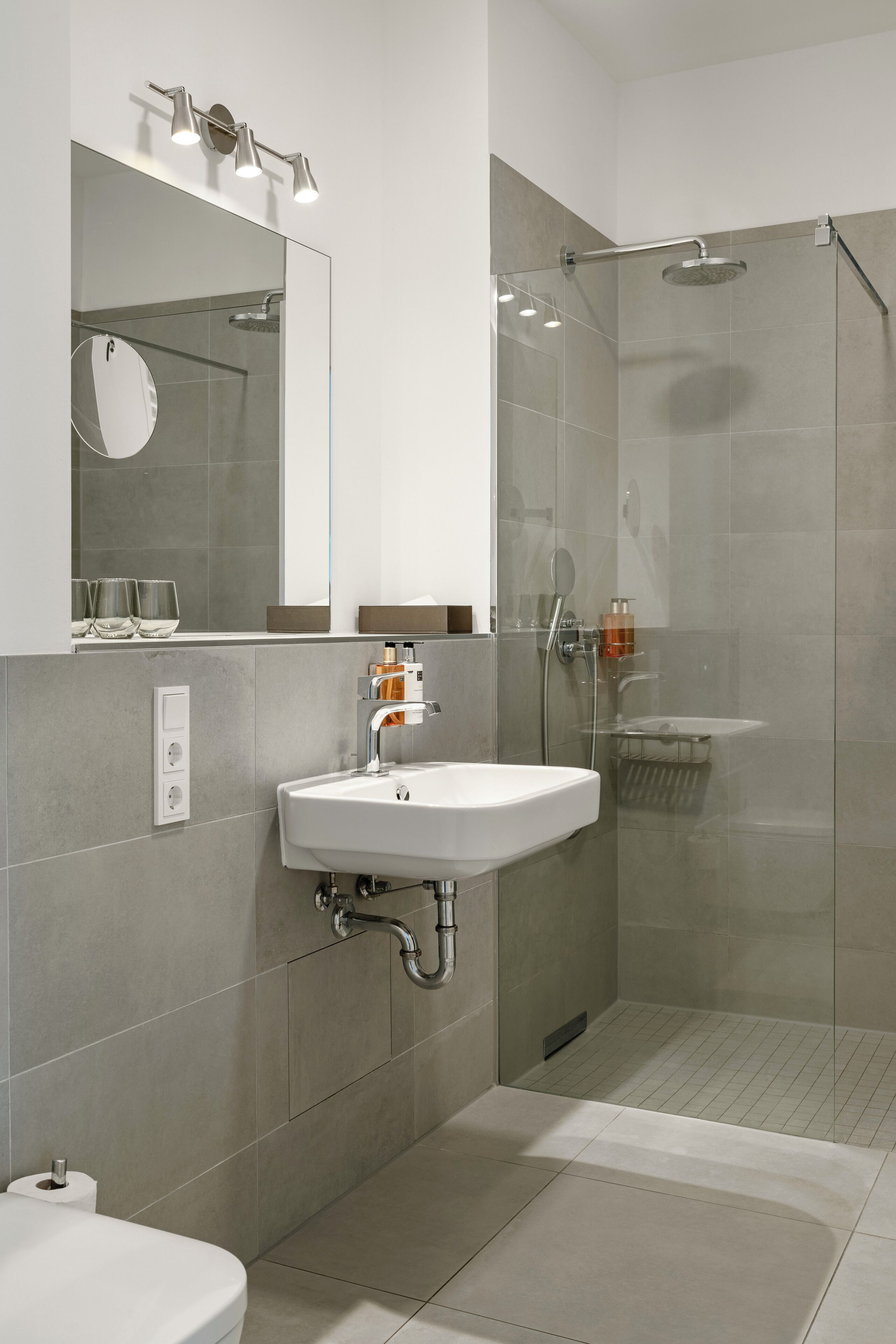 Un baño moderno con una ducha con mampara de vidrio, un lavamanos blanco y un espejo sobre él.