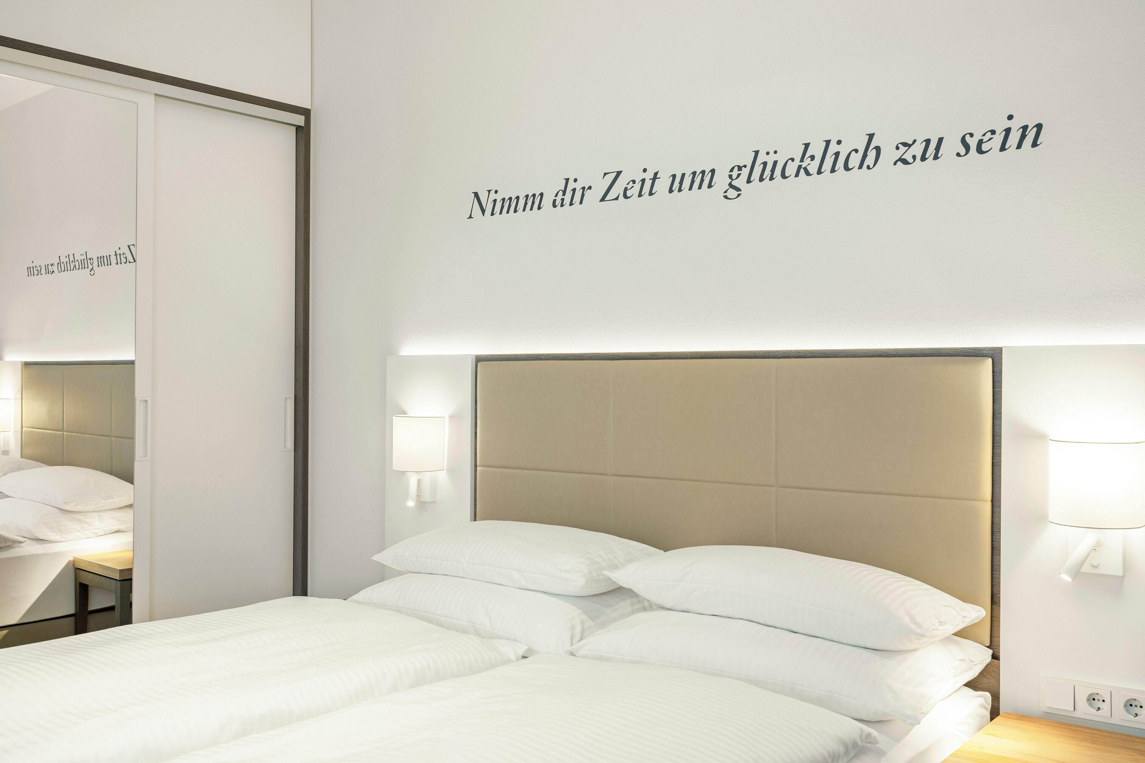 Una habitació d'hotel amb llit, mirall i una paret amb una frase motivacional.