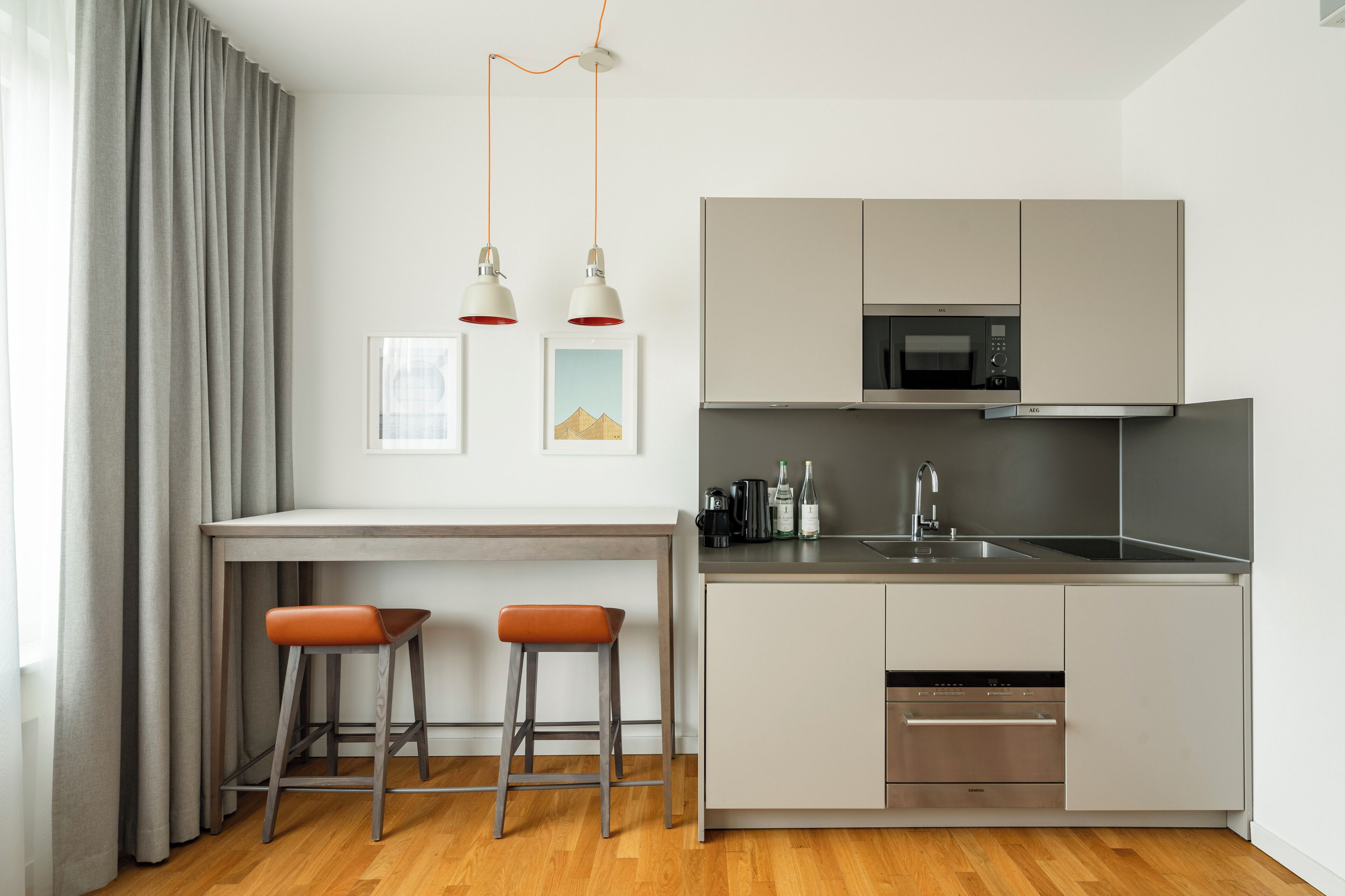 A modern kitchen with a built-in microwave, stainless steel sink, and a dishwasher. There are two stools at the kitchen counter.