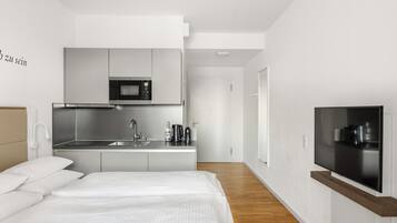 A modern hotel room with a bed, a kitchenette, and a TV.
