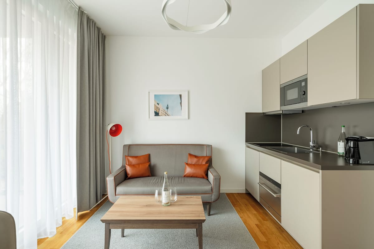 Un salon moderne avec un canapé gris, une table basse en bois et un coin cuisine équipé d’un four à micro-ondes et d’un évier.