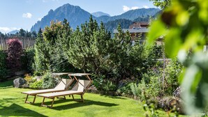 Un jardín con una silla de madera para relajarse, rodeado de vegetación y un telón de fondo de montañas.