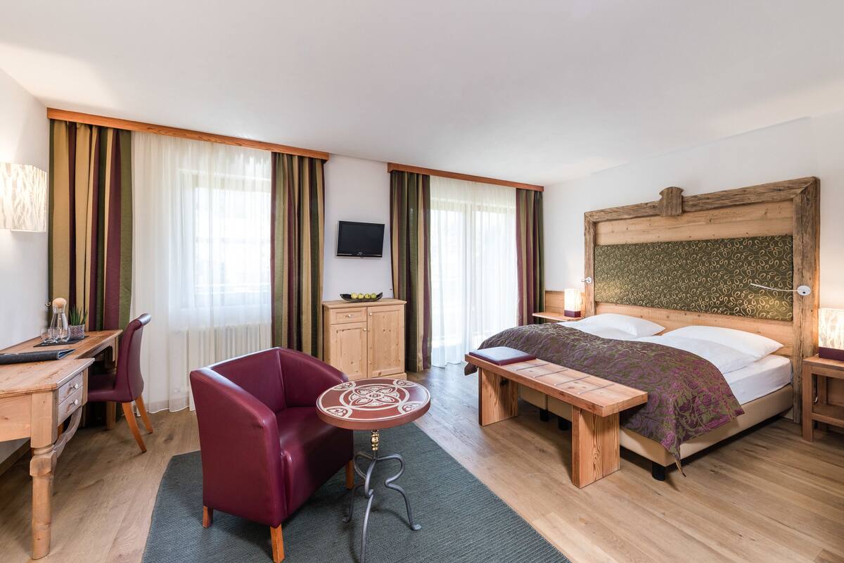 Une chambre d’hôtel avec un lit en bois, un bureau avec une chaise, une petite table et un téléviseur fixé au mur.