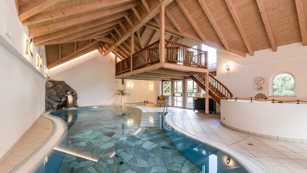 Una amplia piscina interior con techo de madera y pared de piedra.