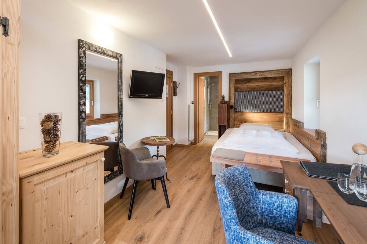 Une chambre d’hôtel moderne avec un plancher en bois, un lit, un bureau avec une chaise, une télévision et un grand miroir.