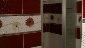 A bathroom with a glass shower enclosure, red tiled walls, and a white tiled backsplash with floral designs. - Hotel Sungur (Demirci)