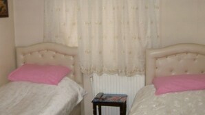 A bedroom with two single beds, each with a pink pillow and a white duvet. There is a small table with a book or magazine on it. - Hotel Sungur (Demirci)