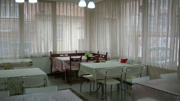 A dining area with tables and chairs, large windows with sheer curtains, and a view of the outside. - Hotel Sungur (Demirci)