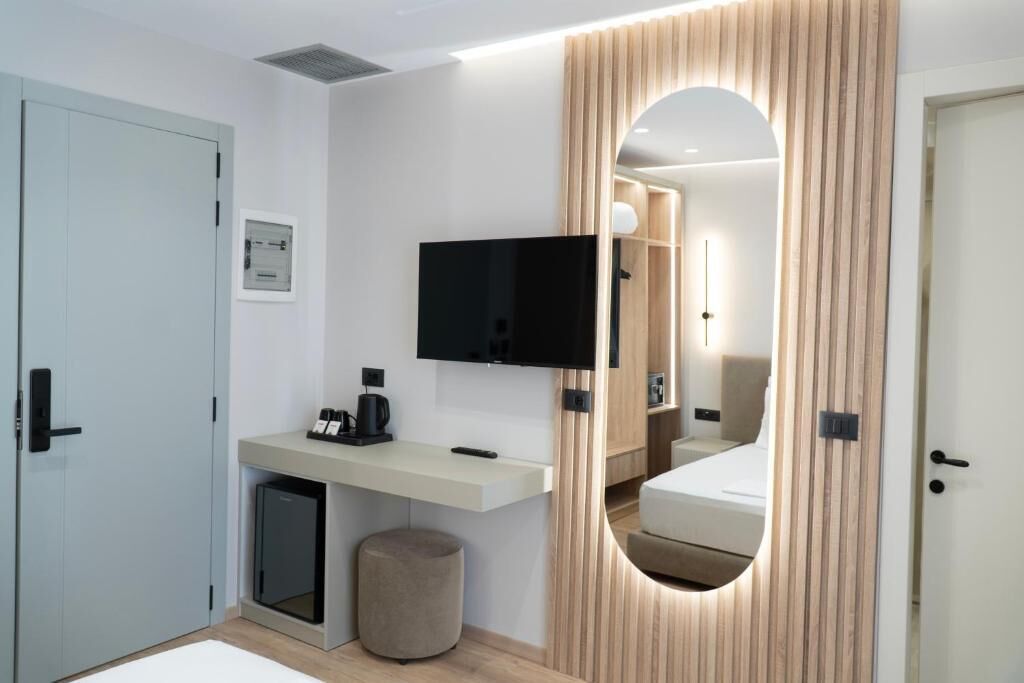 A modern hotel room with a built-in desk, a flat-screen TV, a mirror, and a small seating area.