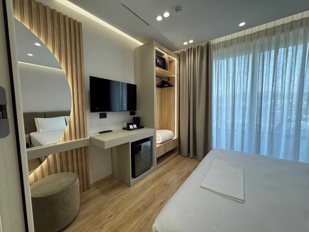 A modern hotel room with a bed, a desk with a flat-screen TV, a seating area, and a wardrobe.