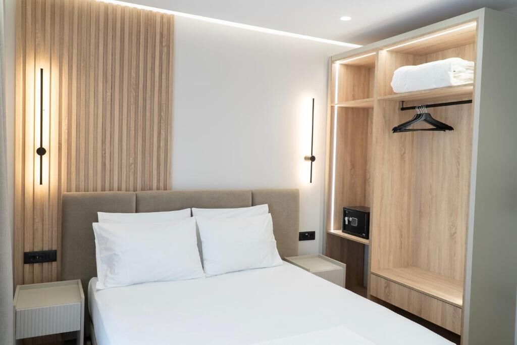 Habitació d'hotel moderna amb un llit, taules de nit, un armari amb espai per penjar roba i una petita taula al costat del llit.