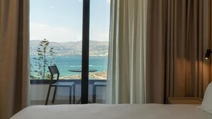 Habitación de hotel con un ventanal grande que ofrece vistas al mar y a la playa.