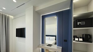 Una habitación de hotel moderna con una cama, un televisor montado en la pared, una mesita de noche con lámpara y una caja fuerte integrada.