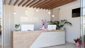 Un mostrador de recepción con terminación de madera y diseño moderno, con dos computadoras portátiles y una planta decorativa.